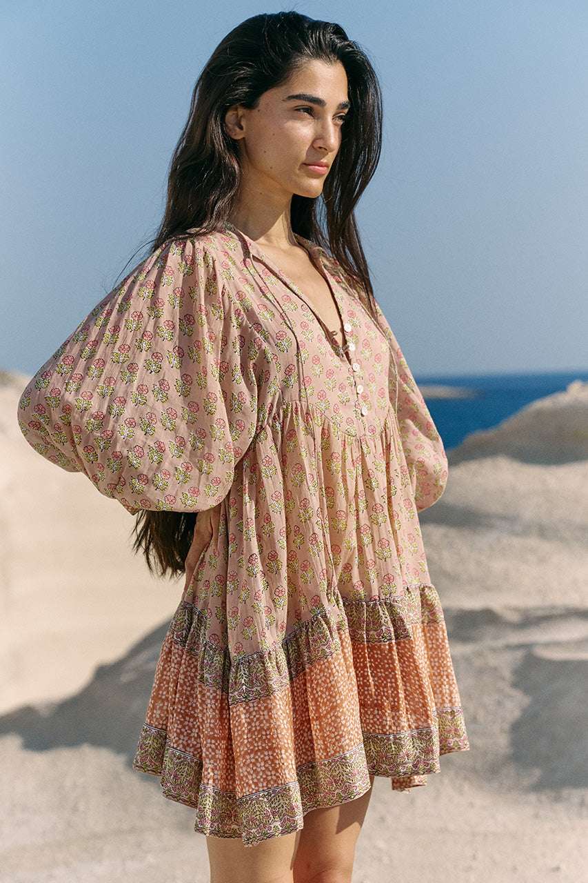 Close-up three-quarter view of woman on sandy beach wearing the Daughters of India Bhoomi Mini Dress in Sunset, showing the dramatic billowed sleeves and open V-neckline
