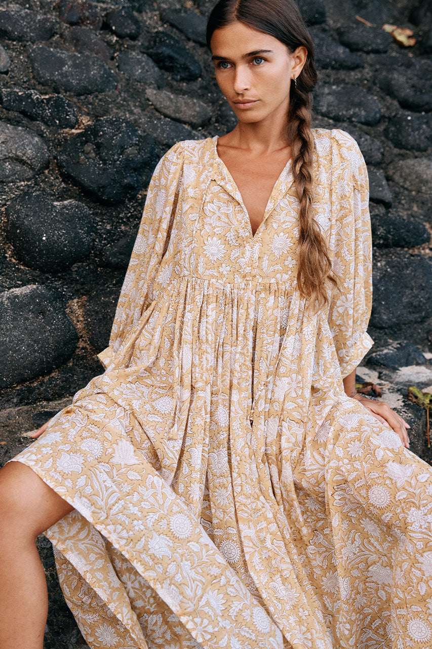 Daughters of India Kyra Midi Dress in Cumin — seated on rocks by beach, V-neckline, flowing hand screen print skirt