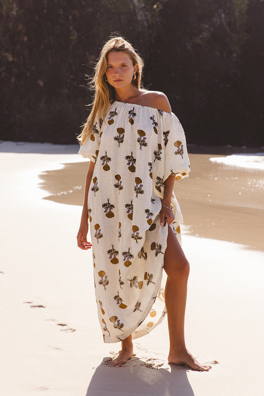 Dahlia Maxi Dress Marigold — full length at beach, off-shoulder, white linen with bold marigold sunflower hand block print, billowy sleeves | Daughters of India