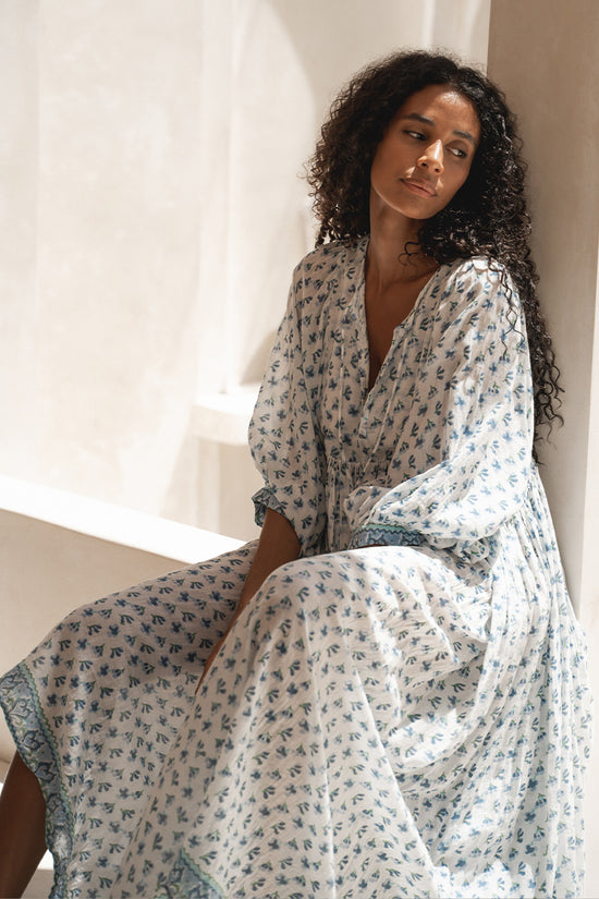 Daughters of India Kyra Maxi Dress in Azure — seated against cream pillar, draped skirt, blue floral block print cotton