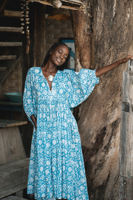 Daughters of India Kyra Midi Dress in Ocean Blue — smiling by wooden post of treehouse, V-neckline, flowing midi
