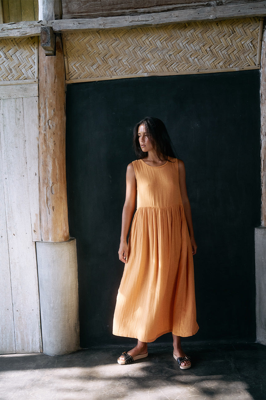 Nadi Dress Amber — full length front view in rustic timber interior, amber double gauze cotton midi dress with gathered skirt, natural light | Daughters of India