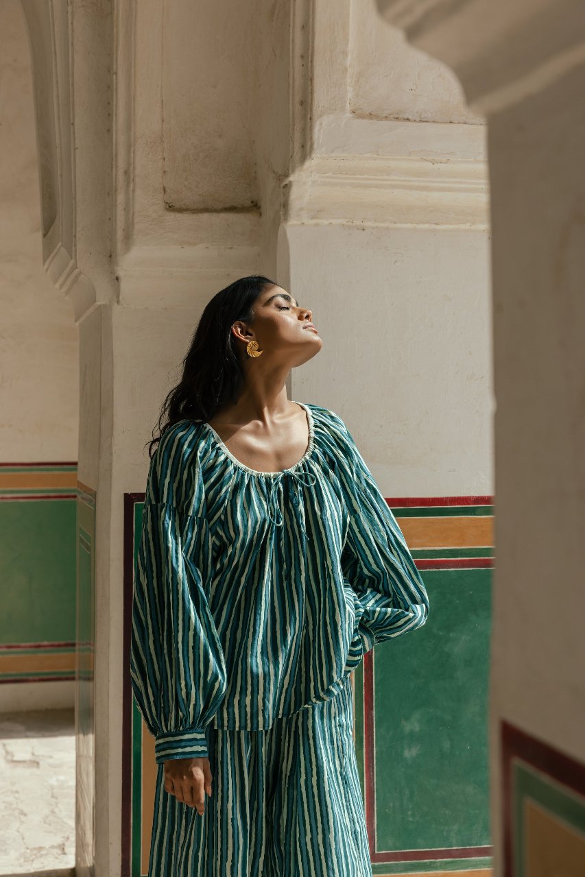 Ria Blouse Cyan Candy — lifestyle doorway portrait, model standing in colourful architectural setting wearing cyan and dark stripe hand block print cotton blouse, artisan Jaipur India | Daughters of India
