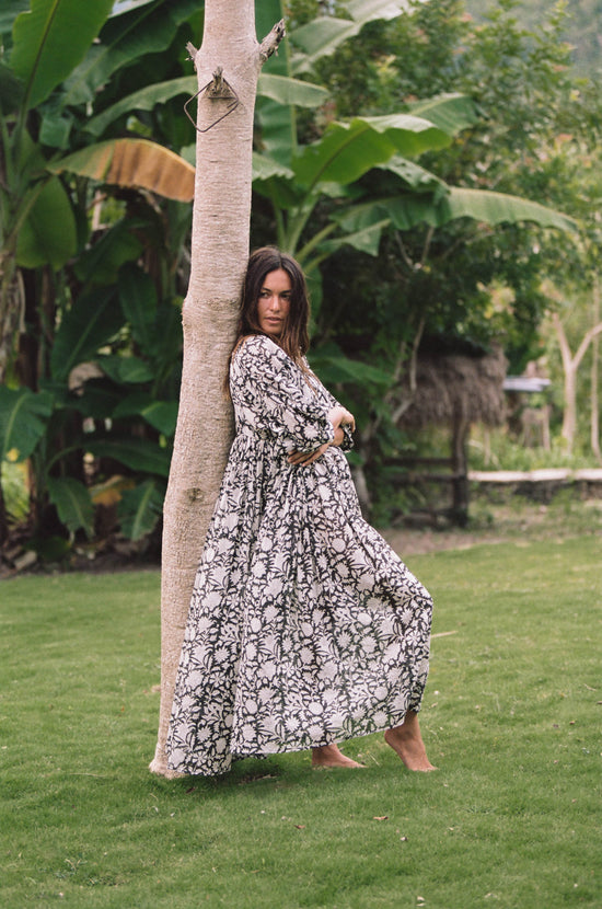 Daughters of India Kyra Maxi Dress in Pepper — leaning against palm tree, flowing skirt, tropical setting